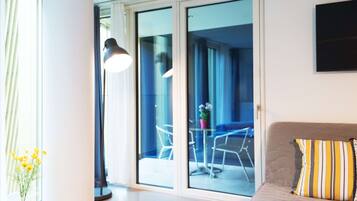 A modern living room with a sofa, a lamp, and a view through a glass door to an outdoor seating area.