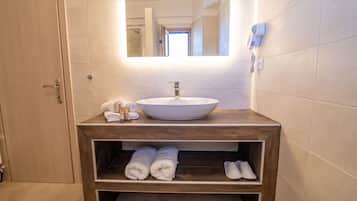 A bathroom with a wooden vanity, a white sink, and a mirror above it. There are towels and a hairdryer on the vanity.
