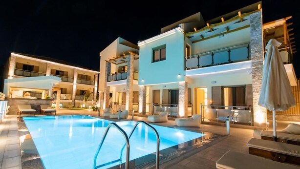 Un hotel moderno con piscina, mobiliario exterior e iluminación en la fachada.