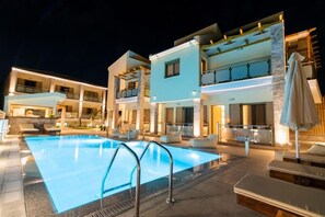 Un hotel moderno con piscina, mobiliario exterior e iluminación en la fachada.