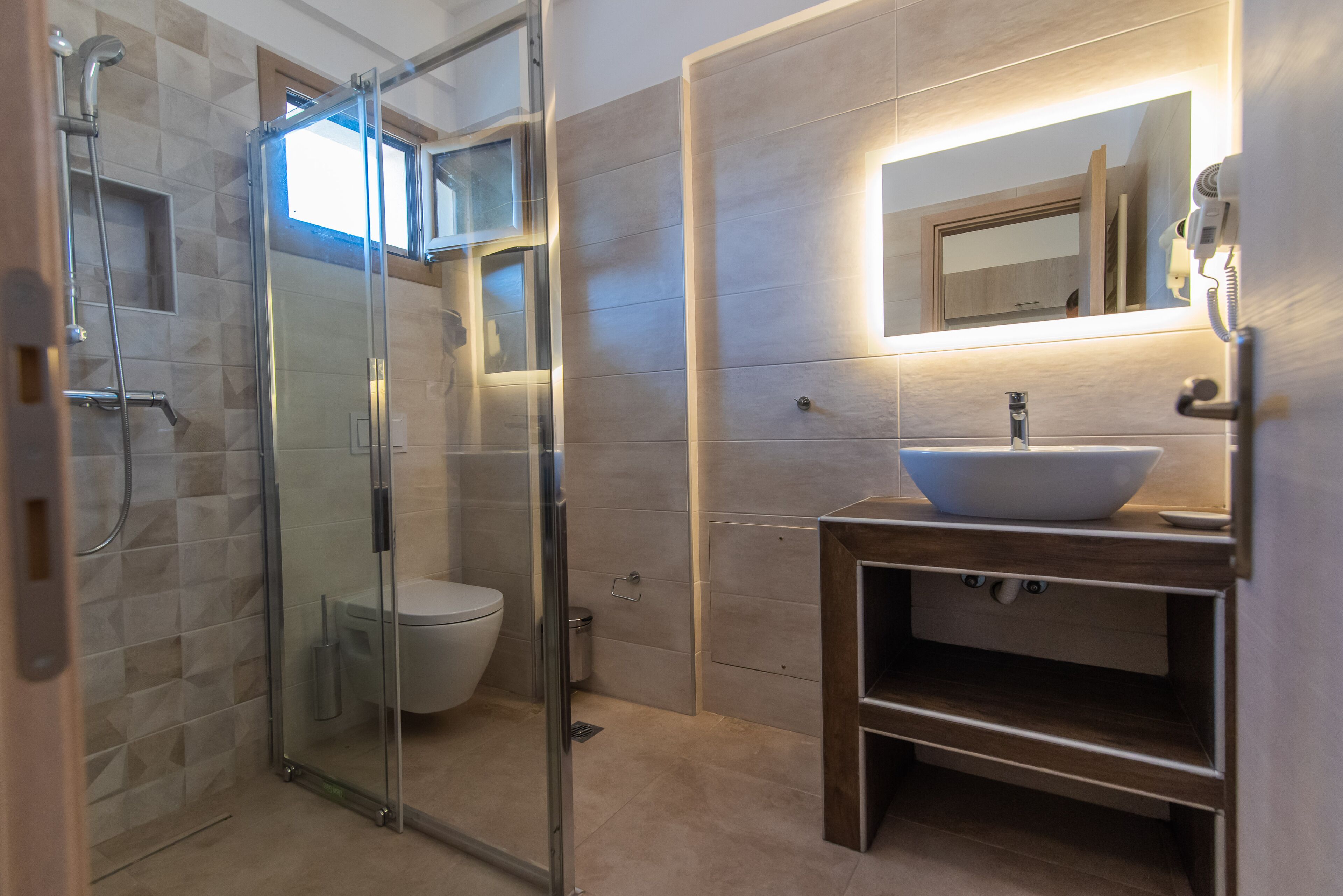 A modern bathroom with a glass-enclosed shower, a white toilet, and a wooden vanity with a large mirror.