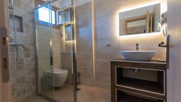 Un baño moderno con ducha envuelta en vidrio, inodoro blanco y tocador de madera con un espejo grande.