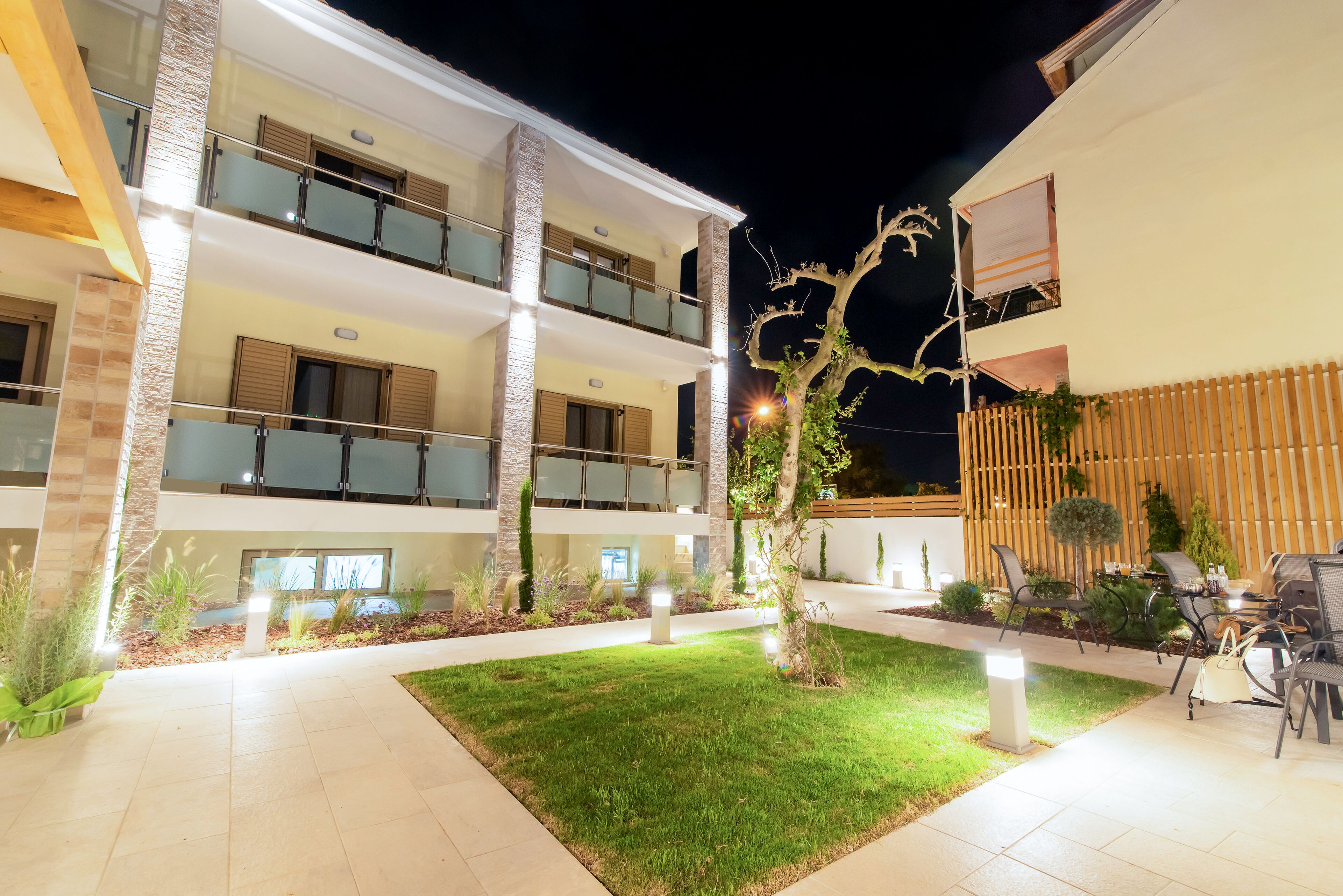 Un edificio de varios pisos con balcones, un patio bien iluminado y mesas al aire libre.