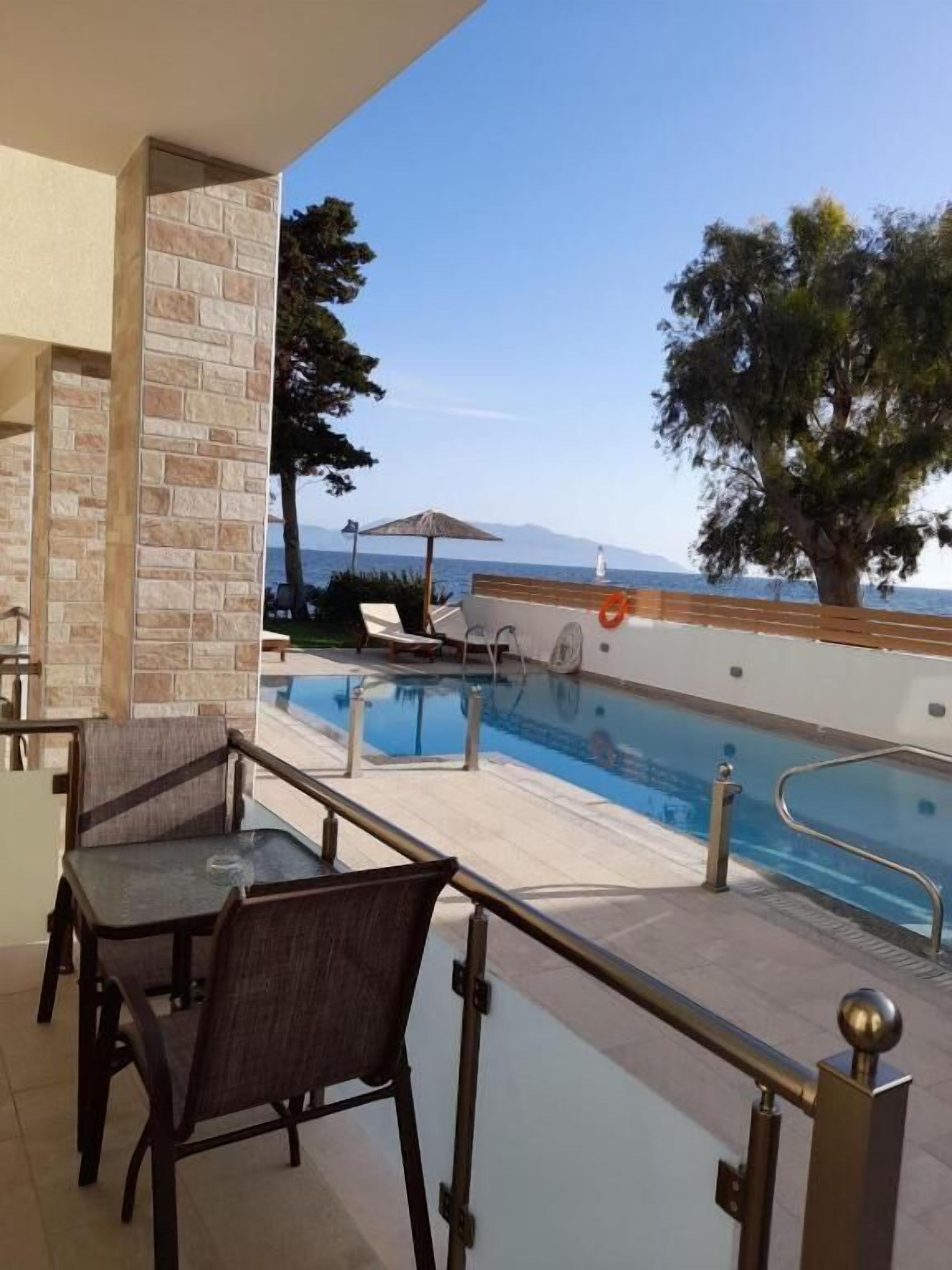 A poolside area with a view of the sea, a lounge chair, and a table.