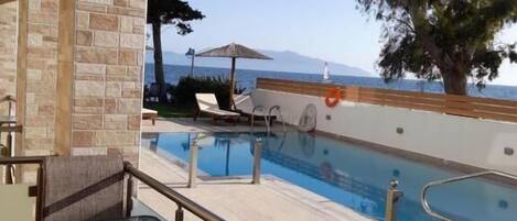 A poolside area with a view of the sea, a lounge chair, and a table.