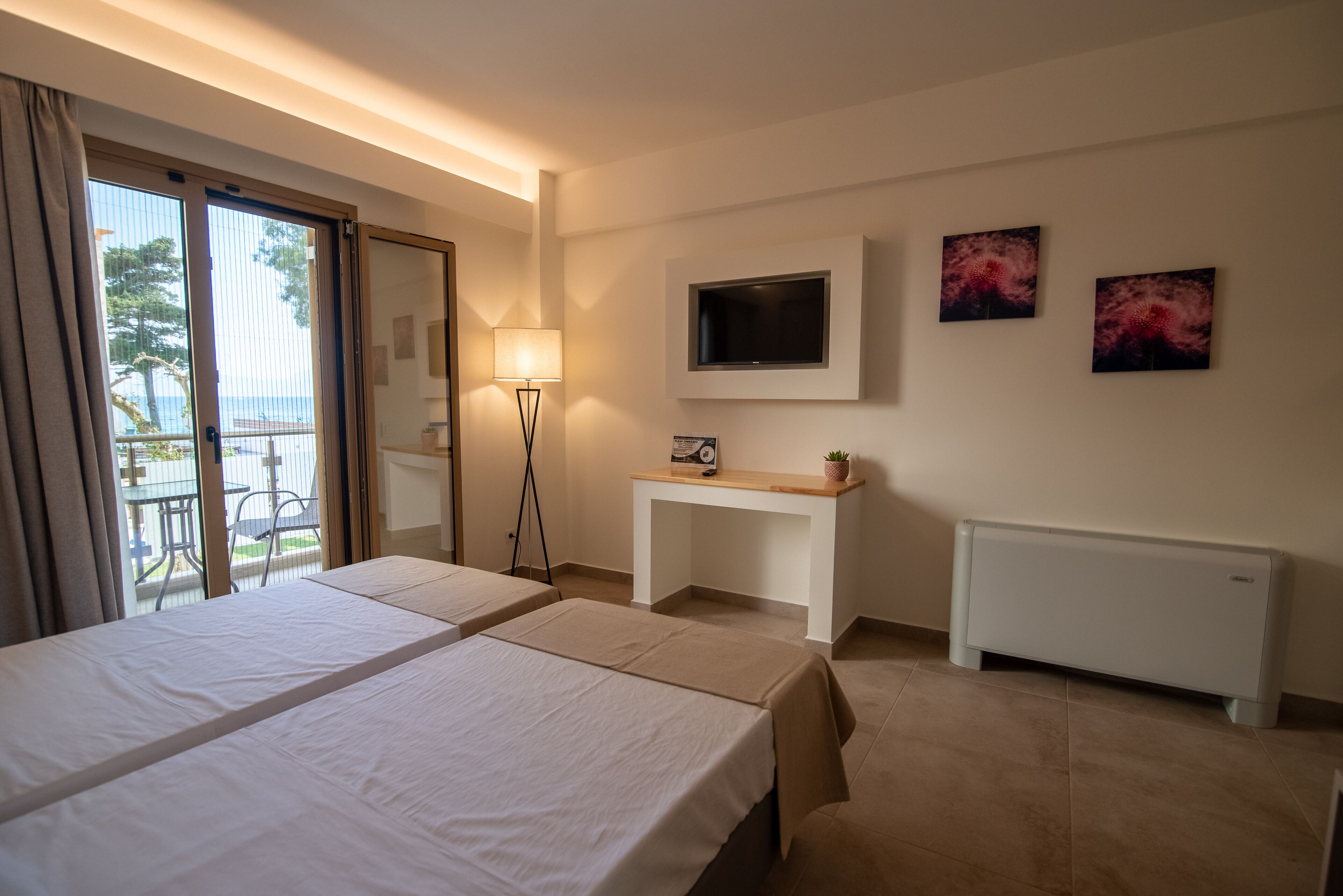 A hotel room with two beds, a TV mounted on the wall, a small table, and a radiator.