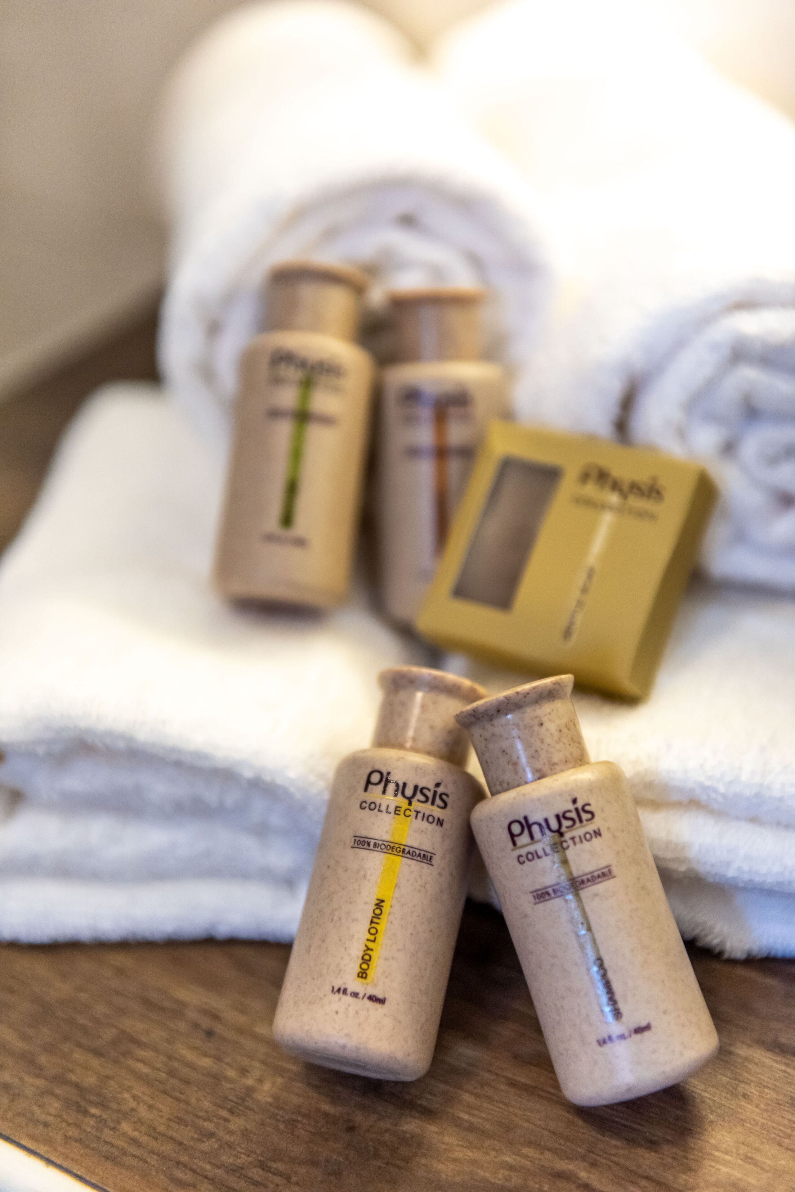 Un ensemble de produits de toilette comprenant une lotion pour le corps et un savon, disposés sur une surface en bois, avec une serviette blanche en arrière-plan.