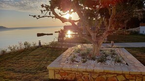 Una jardinera de piedra con un árbol, un camino y vista al mar al atardecer.