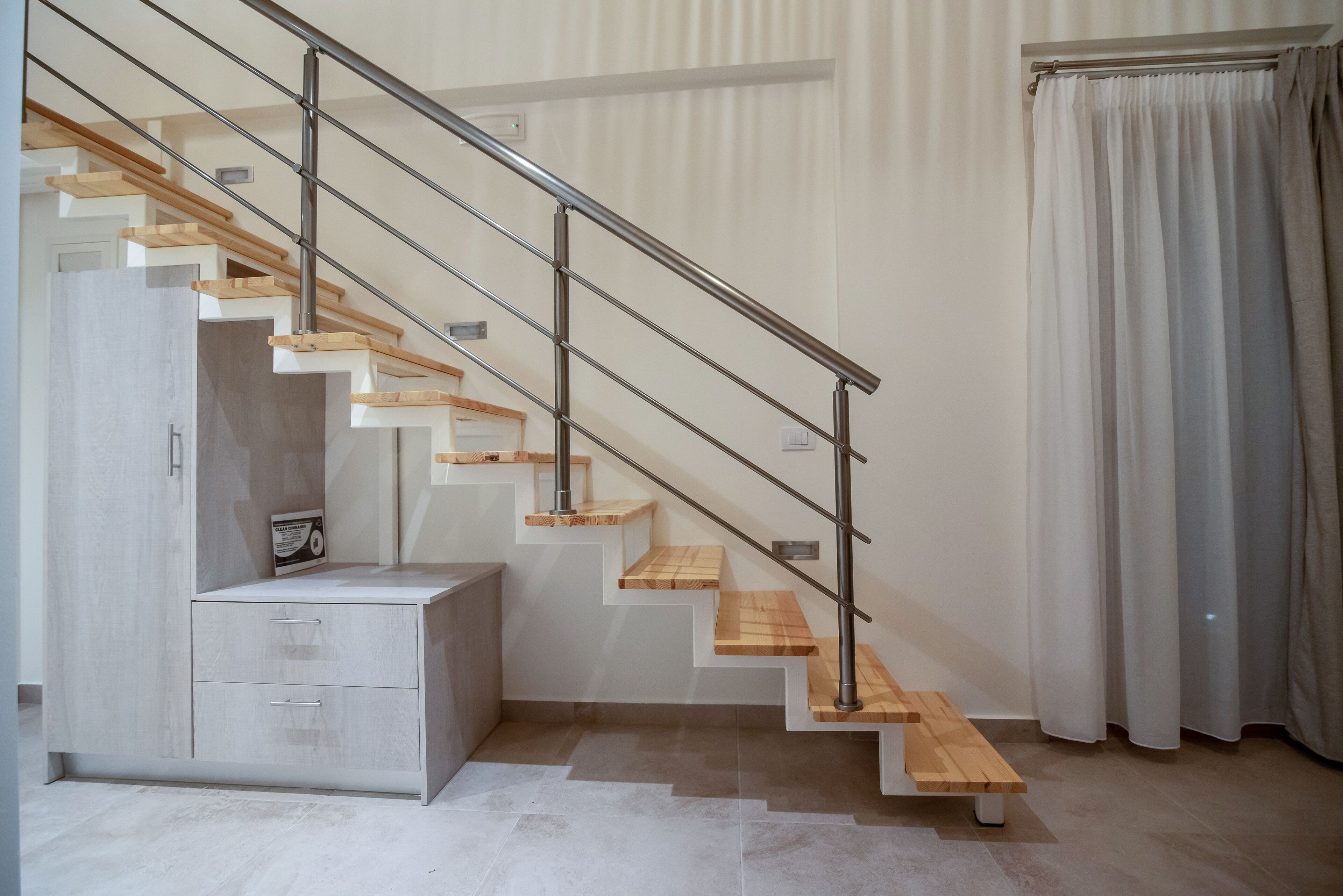 Una escalera moderna con escalones de madera y barandillas de metal, que conduce a un rellano con una zona de estar pequeña y un armario.
