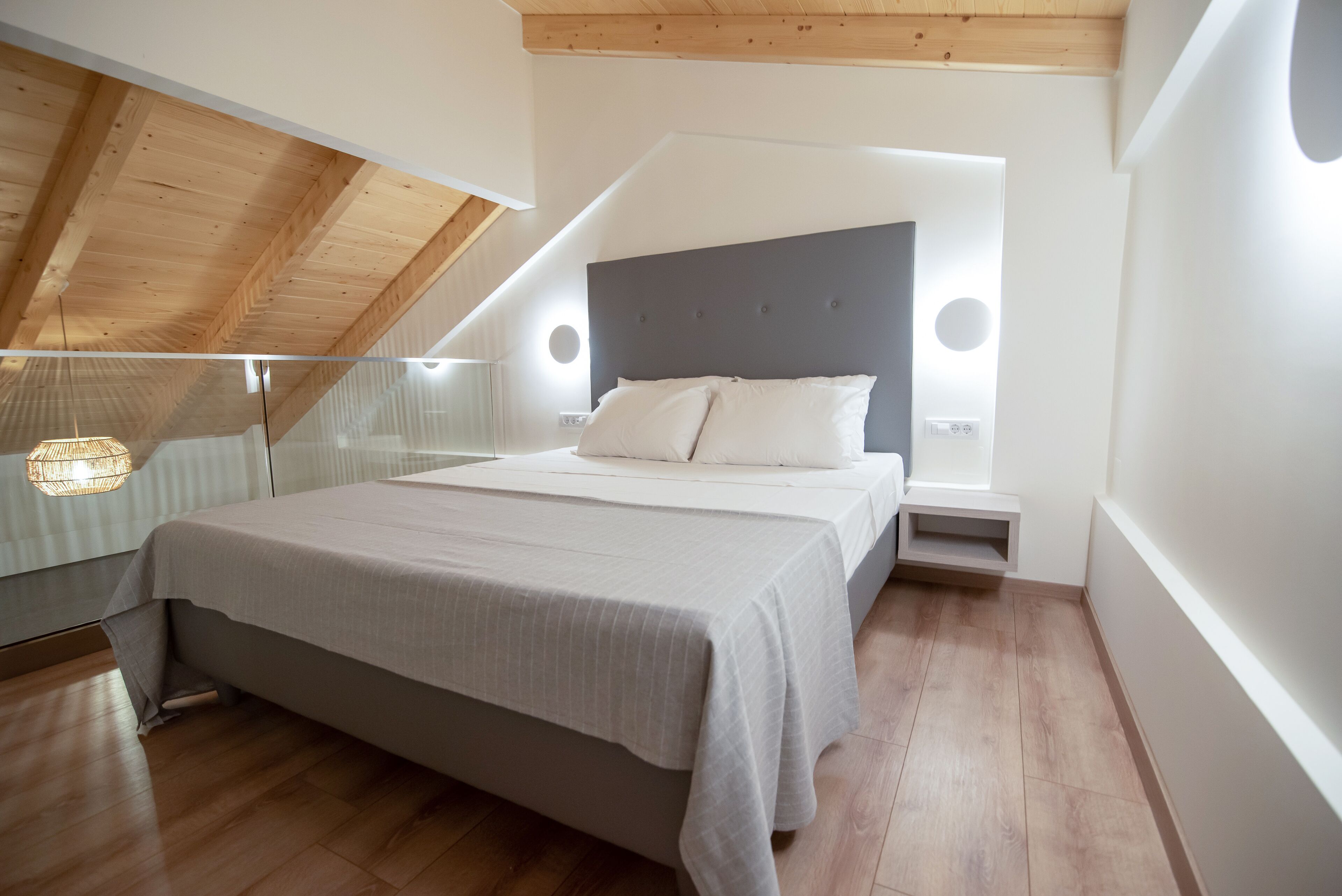 Ein modernes Schlafzimmer mit schrägen Wänden, einem großen Bett mit grauem Kopfteil und Nachttischen mit integrierter Beleuchtung.