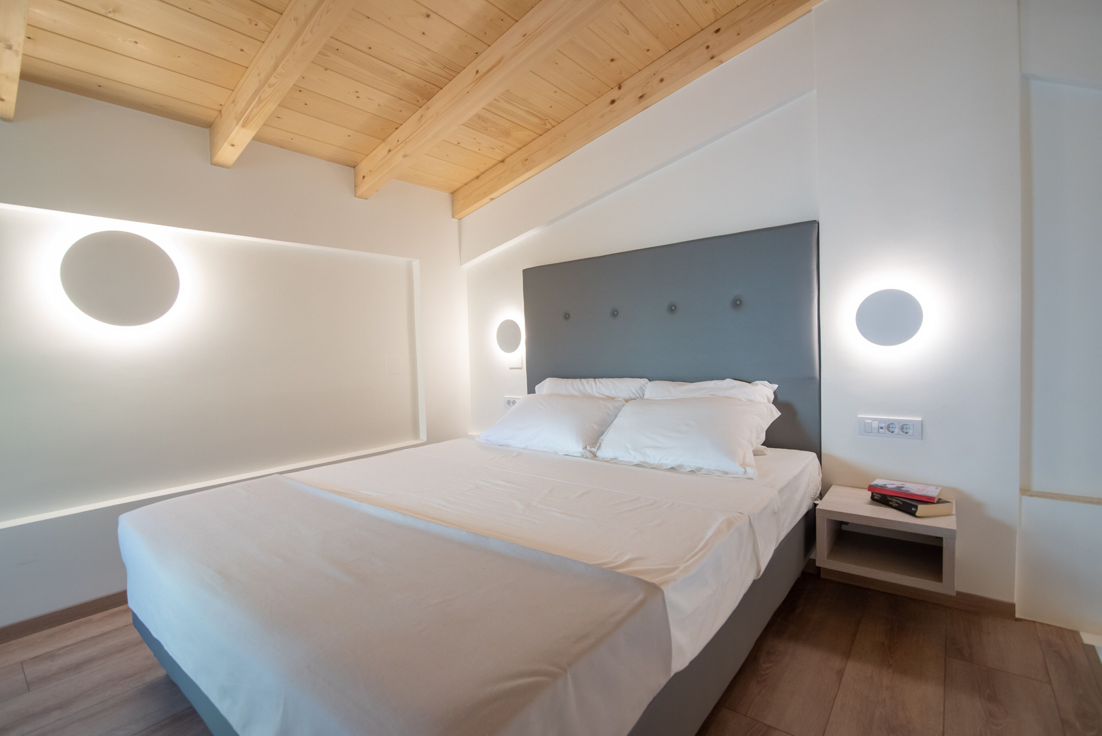 Ein modernes Schlafzimmer mit einem großen Bett, runden Wandleuchten und einer Holzbalkendecke.