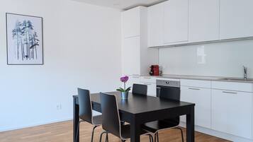 Una cocina moderna con armarios blancos, un comedor con mesa negra y cuatro sillas, y una pequeña planta en maceta sobre la mesa.