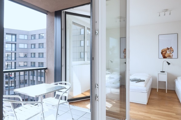 A modern bedroom with a glass door leading to a balcony, a bed, a small bedside table, and a framed picture on the wall. - Hitrental Basel Apartments (Basel)
