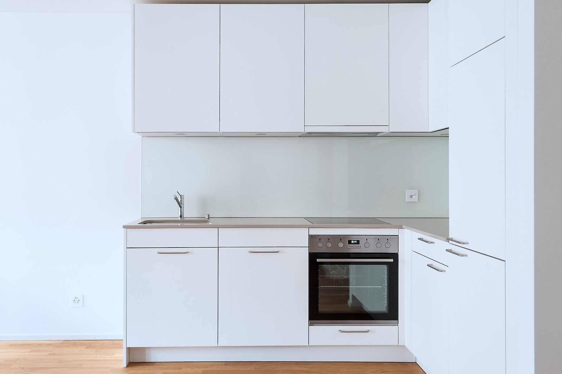 A modern kitchen with white cabinets, a built-in oven, and a stainless steel faucet.