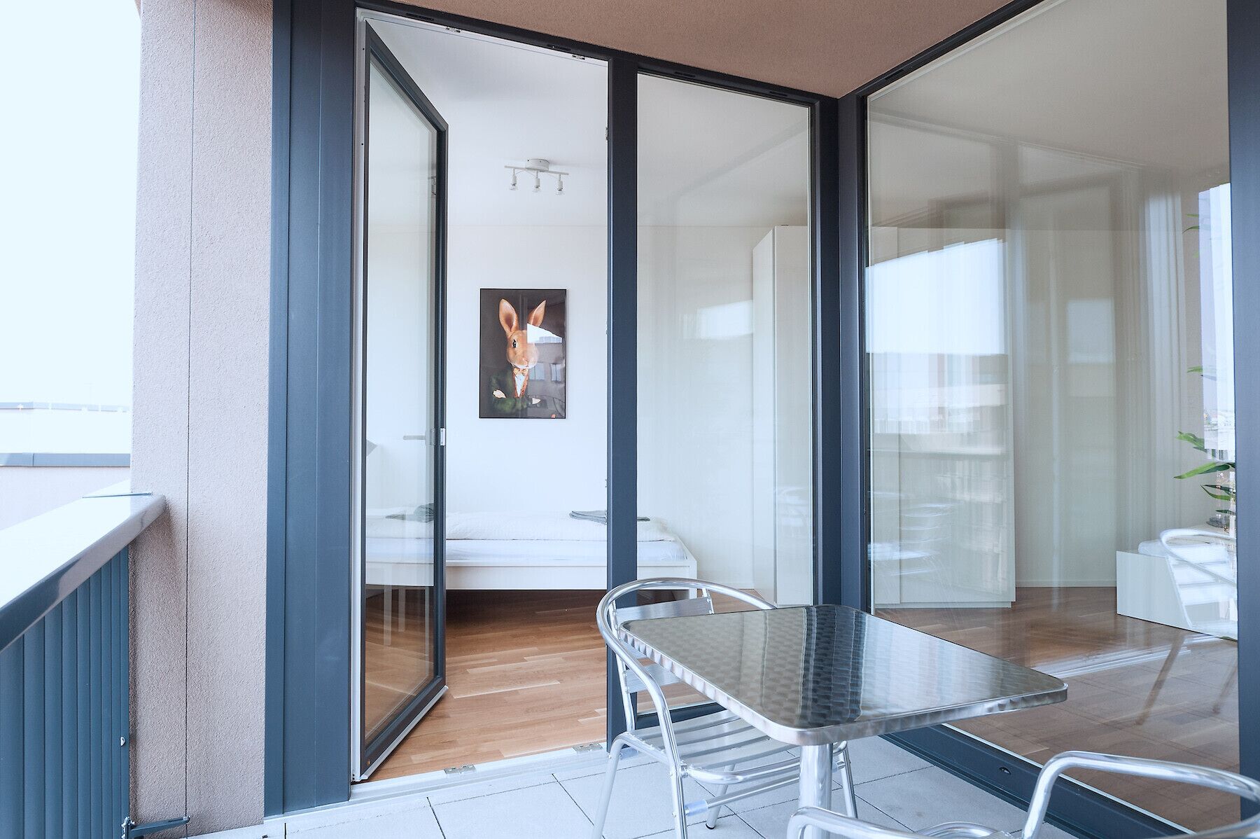 A modern room with a glass door leading to a balcony, a bed, a table, and a chair.