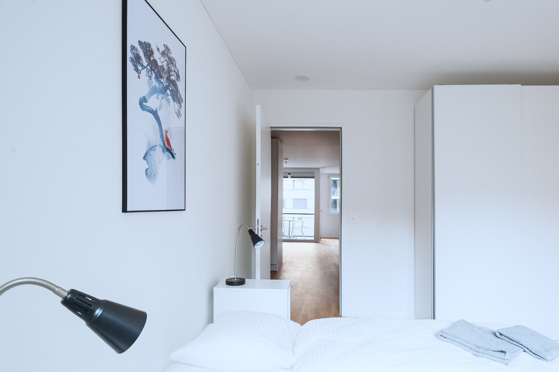 Une chambre moderne avec un lit, un bureau et une chaise. Une porte donne accès à une autre pièce.