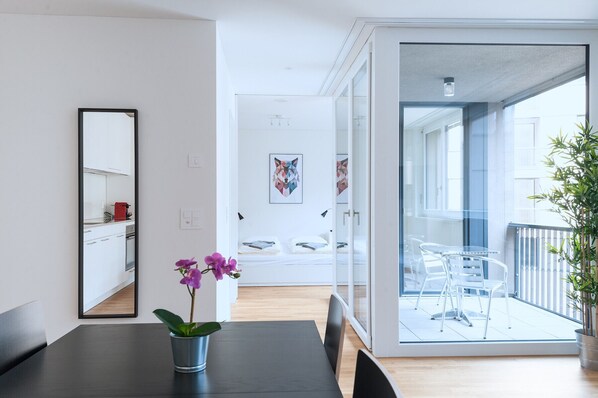 Un interior moderno con zona de comedor, cocina y balcón con puertas de vidrio transparente.