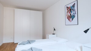 Ein schlicht eingerichtetes Schlafzimmer mit einem großen Bett, einem Nachttisch, einer Lampe und einem geometrischen Kunstwerk an der Wand.