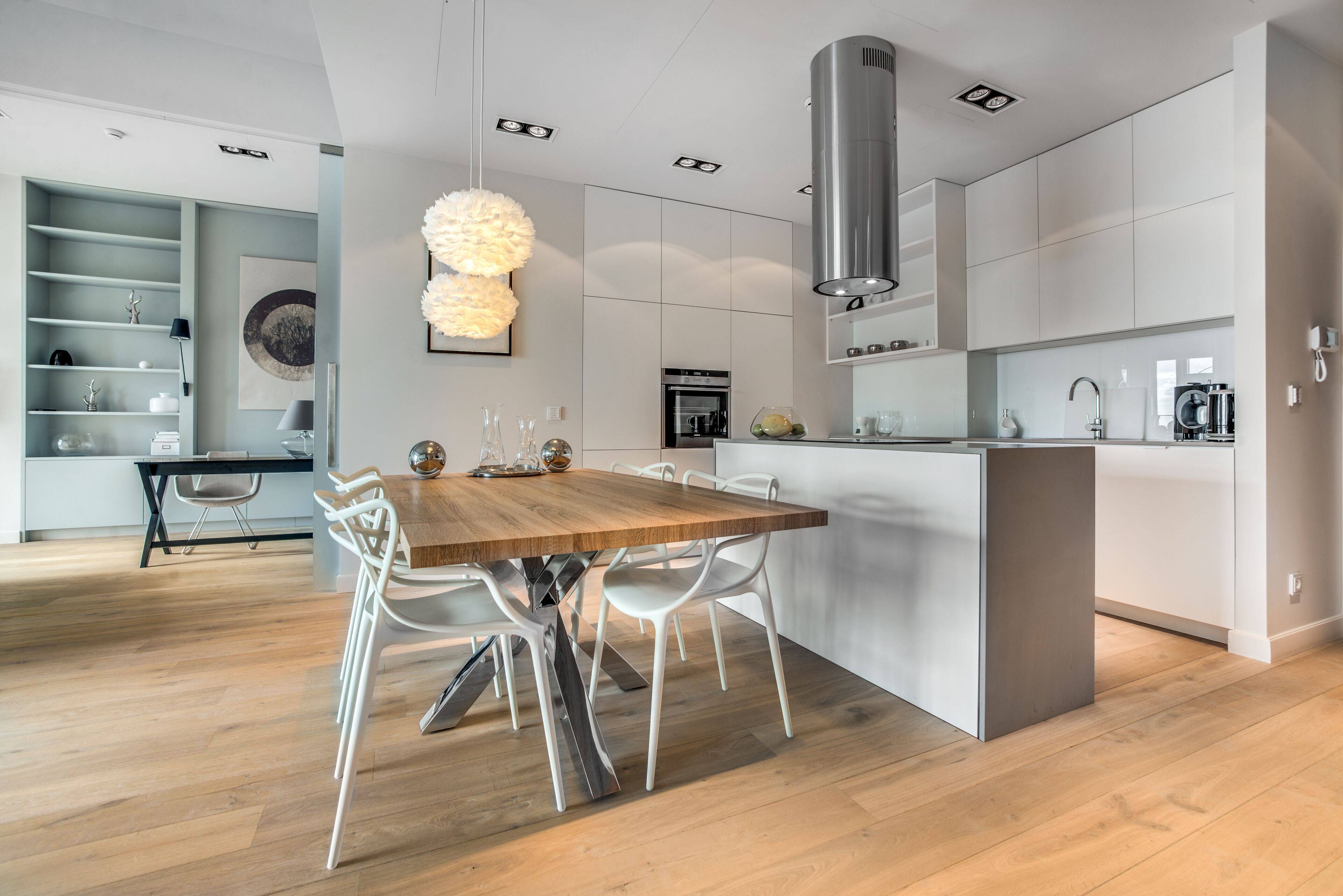 Una cocina moderna con una mesa de comedor de madera, sillas blancas y electrodomésticos integrados.