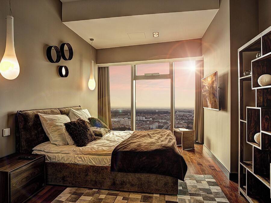A modern bedroom with a large bed, city view, and a wooden bookshelf.