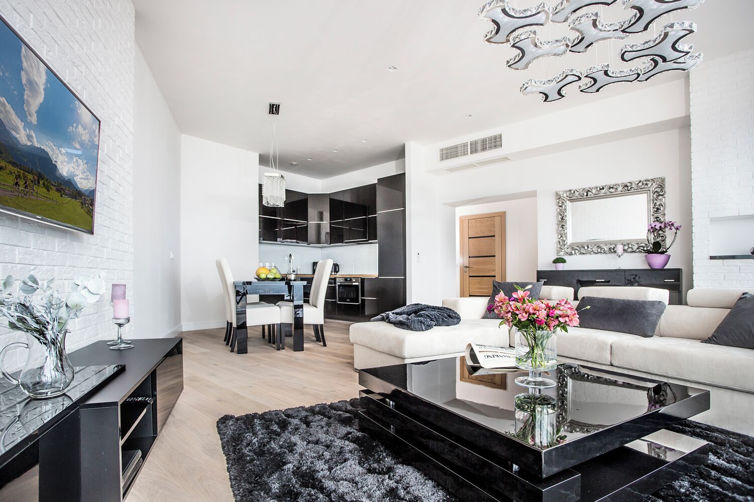 Una sala moderna con una mesa de centro de mármol negro, un jarrón de cristal con flores, un sofá blanco y una zona de comedor con mesa y sillas negras.