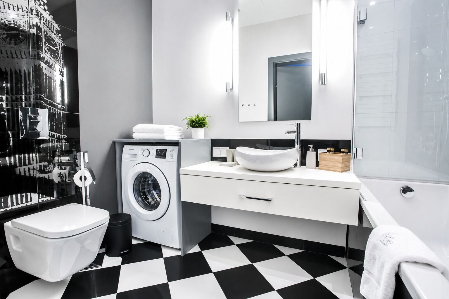 Een moderne badkamer met een zwart-wit schakeerd vloer, een wasmachine, een wastafel met een waskom en een toilet.