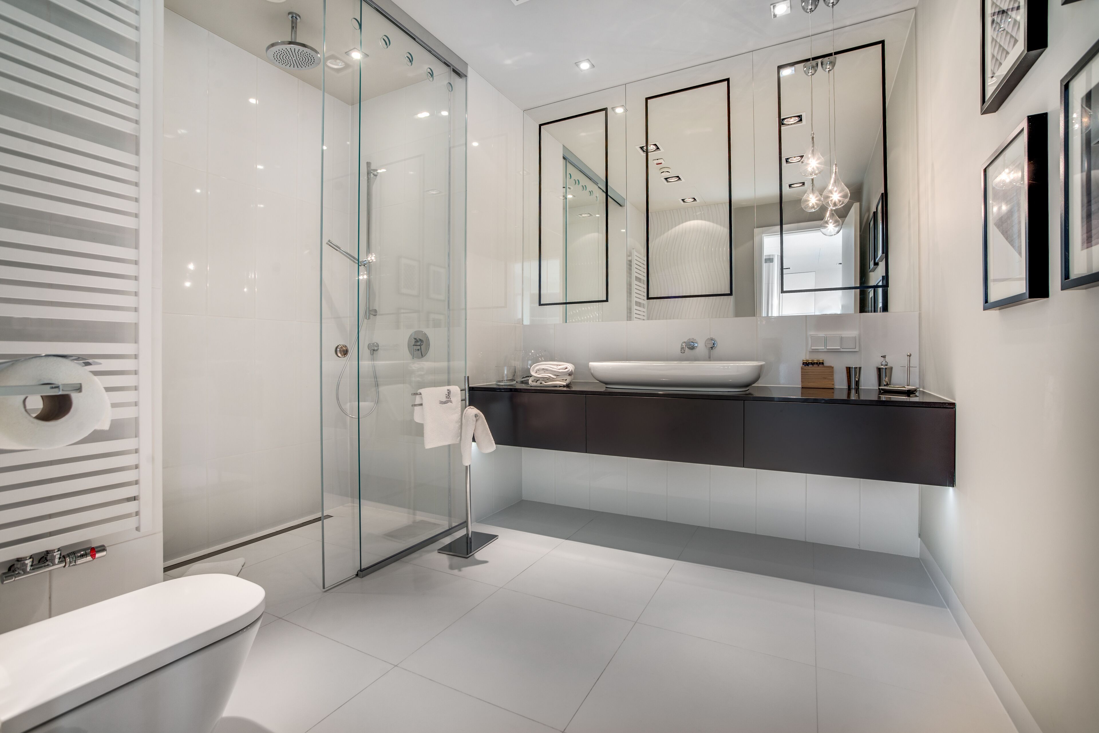 Een moderne badkamer met een douchecabine van glas, een wit toilet en een grote spiegel boven een donker aanrecht.