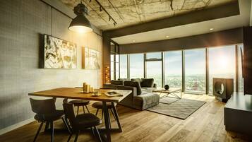 A modern living room with a wooden dining table, chairs, a sofa, and a large window offering a city view.