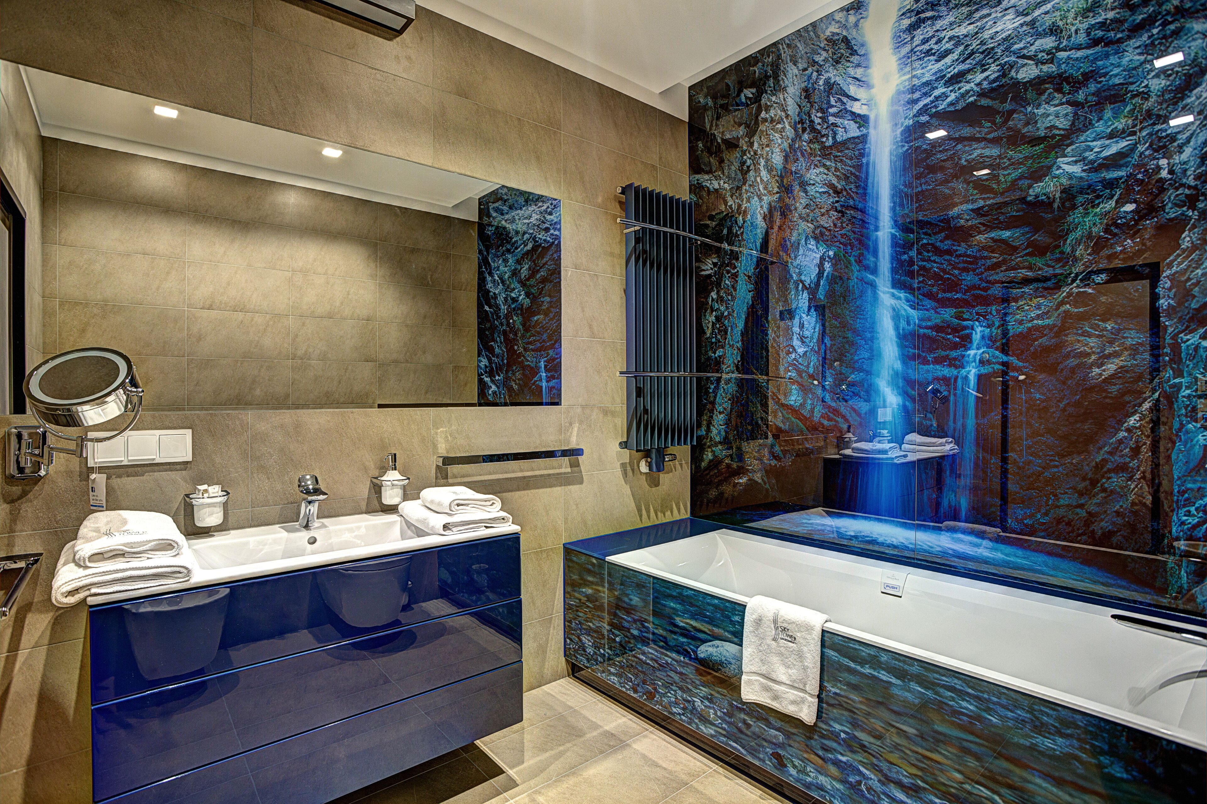 Une salle de bain moderne dotée d’un grand miroir, d’un meuble-lavabo à deux vasques et d’une grande baignoire avec un système de cascade d’eau.