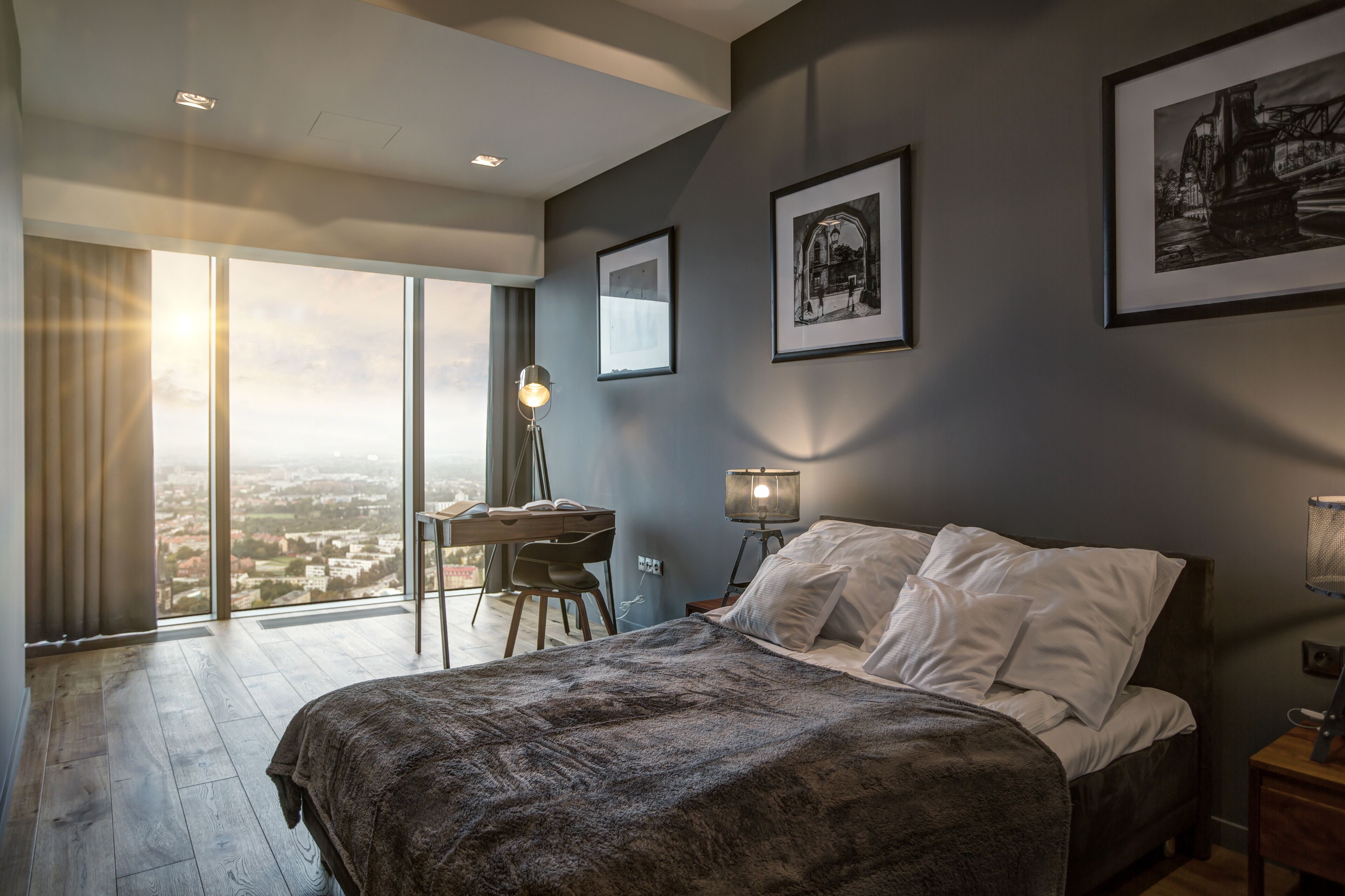 A modern bedroom with a large bed, a desk, and a view of the city.