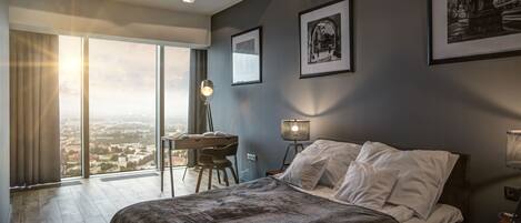 A modern bedroom with a large bed, a desk, and a view of the city.