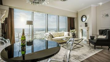 A spacious living room with a large window, a round glass table, a sofa, and a black leather armchair.