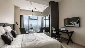 A modern hotel room with a large bed, a desk, a chair, a TV, and a city view.