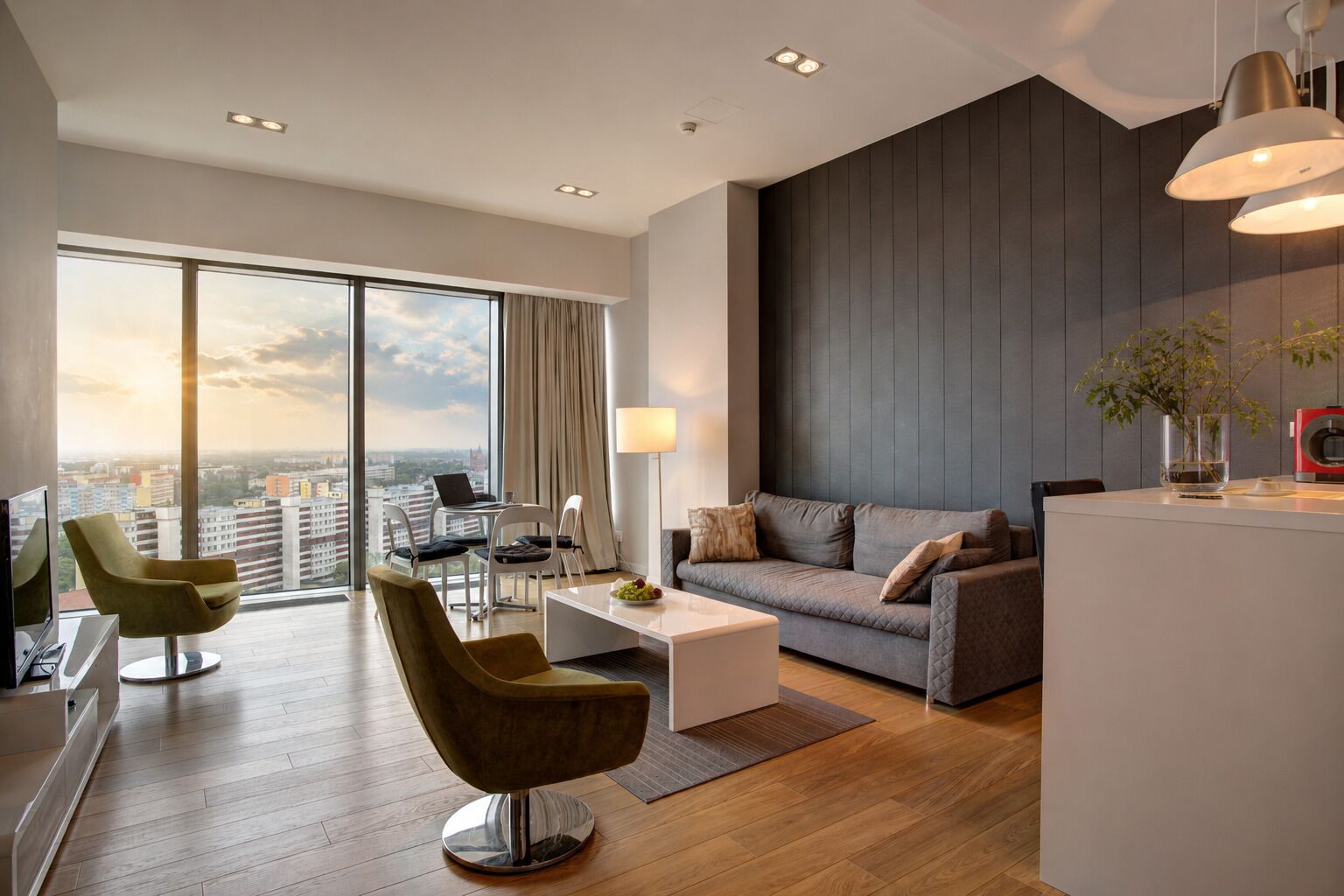 Et moderne hotelværelse med et stort vindue, en sofa, et sofabord, et fjernsyn og et skrivebord med en bærbar computer.