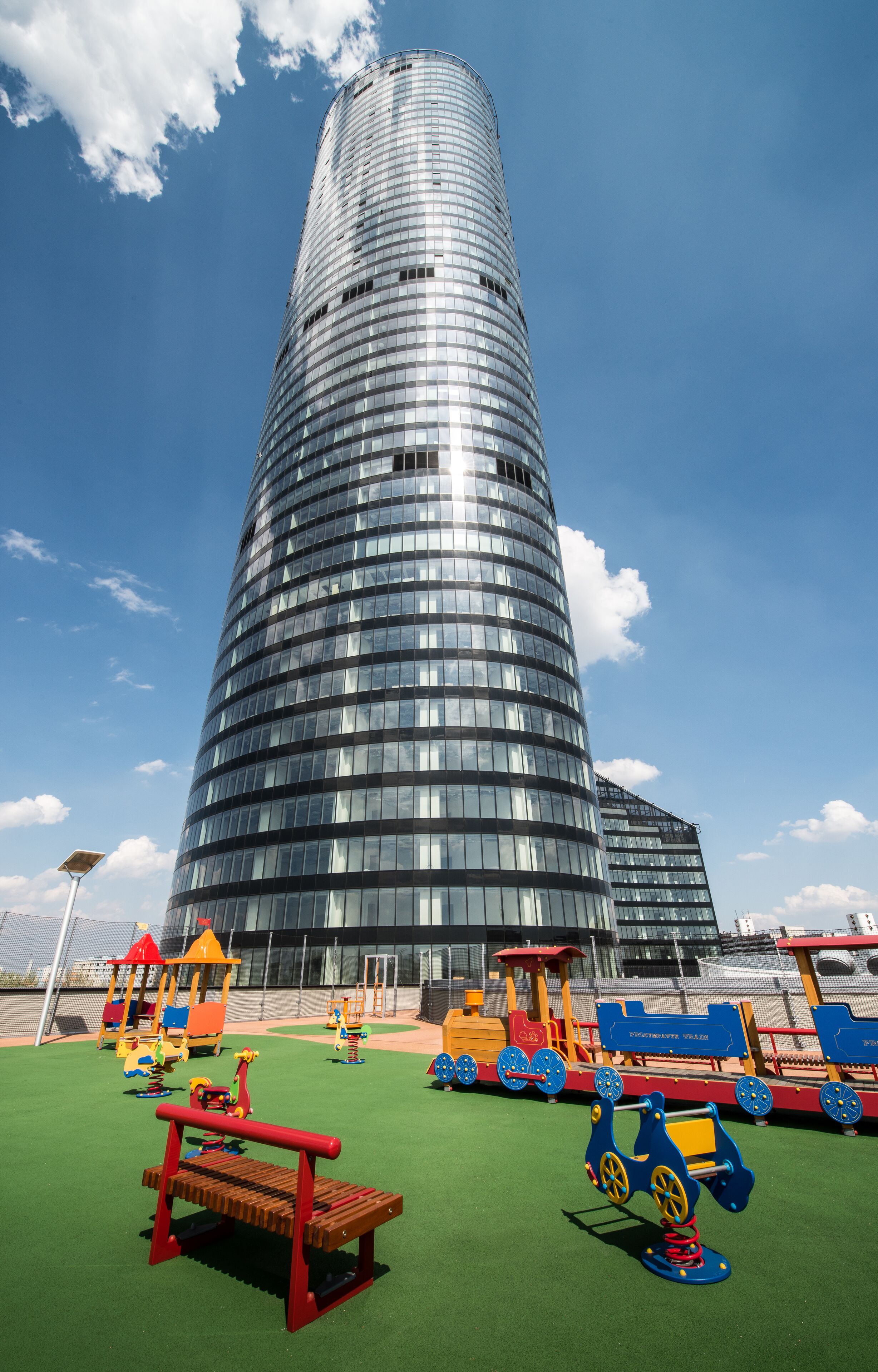 Un edificio moderno con fachada curva y un parque infantil con juegos de colores delante.