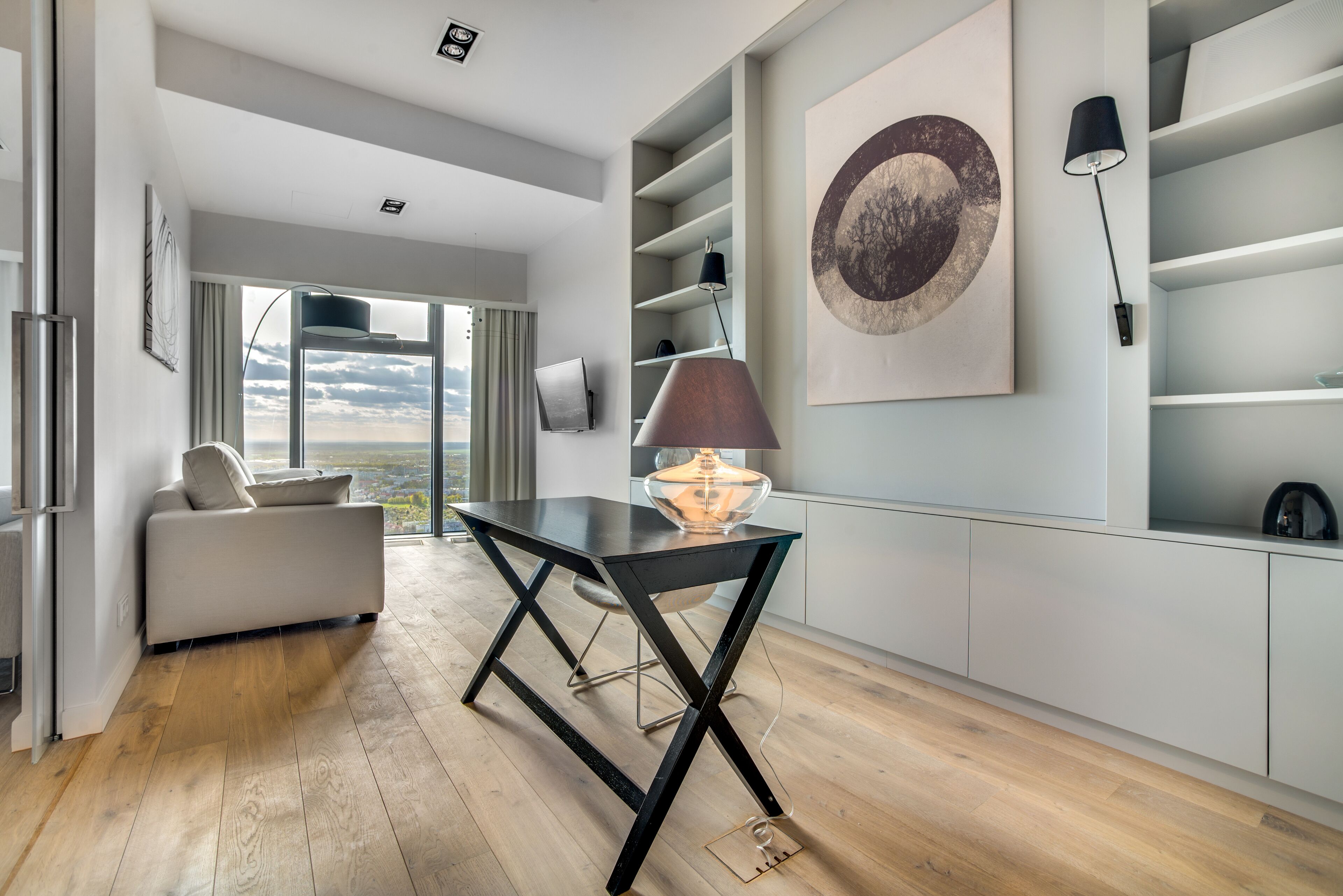 Uma sala de estar moderna com uma mesa de centro de vidro, um sofá e uma janela grande com vista para o céu.