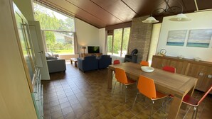 Amplia sala de estar con una mesa de comedor de madera, sillas anaranjadas, un sofá y un televisor.