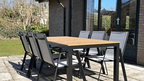 Una mesa de patio con cuatro sillas, un muro de ladrillo y una puerta de cristal con una cruz.