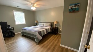 A bedroom with a bed, two bedside tables with lamps, a ceiling fan, a window with blinds, and a wall sign. - Sunset On The Water! (Port Clinton)