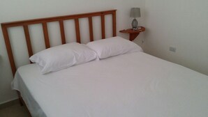 Een eenpersoonsbed met een houten hoofdeinde, wit beddengoed en een nachtkastje met een lamp en telefoon.