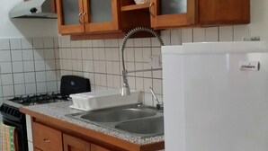 Een keuken met houten kastjes, een RVS spoelbak, een gasfornuis en een witte koelkast.