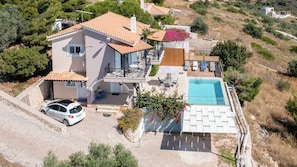 Una casa de dos pisos con piscina, un coche aparcado en la entrada y un muro de piedra.