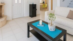 A living room with a sofa, a coffee table with a plant, a fireplace, and a door leading to a kitchen. - Coastal Paradise Found - Komis' Private Pool Gem (Agios Nikolaos)