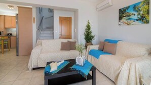 A living room with a sofa, a coffee table, and a painting on the wall. - Coastal Paradise Found - Komis' Private Pool Gem (Agios Nikolaos)