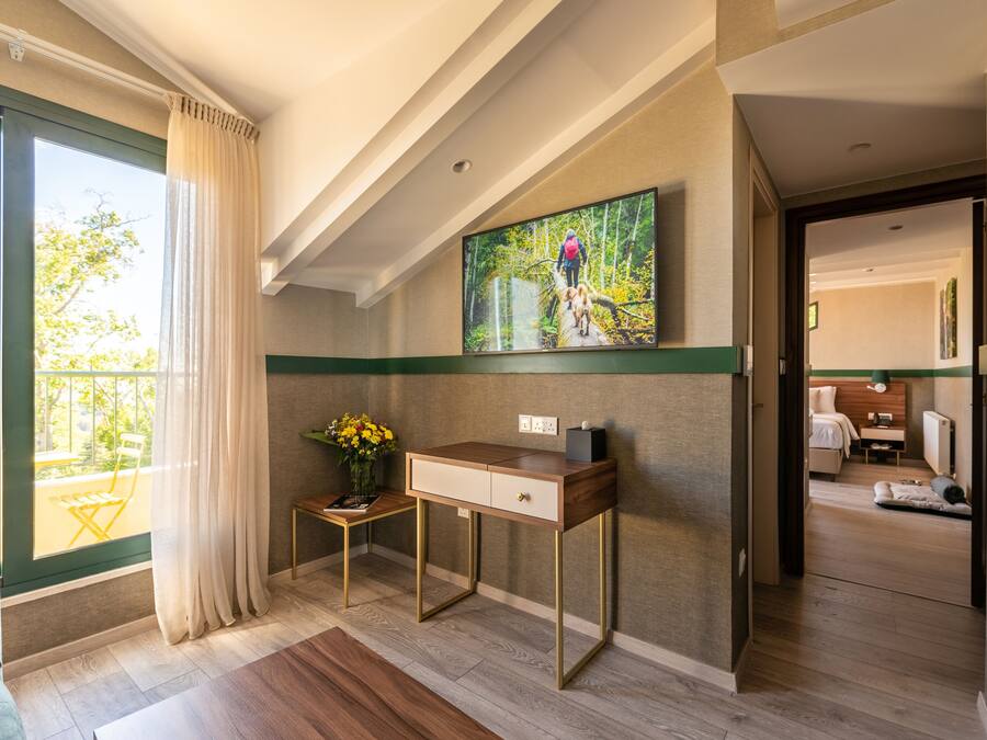 Una habitación de hotel moderna con un ventanal grande, un escritorio con un florero y un cuadro en la pared.
