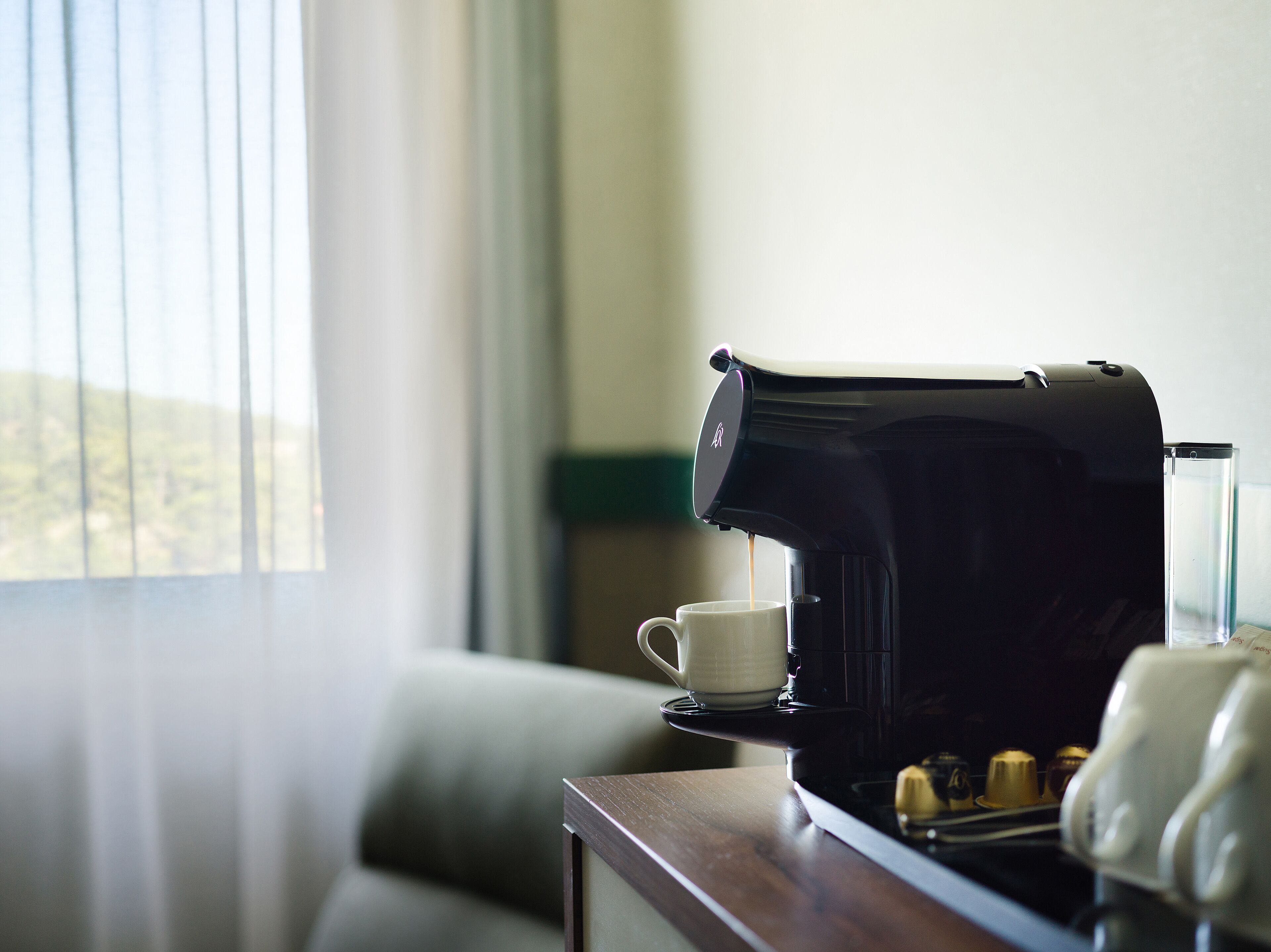 A coffee maker on a table with a cup and a glass.