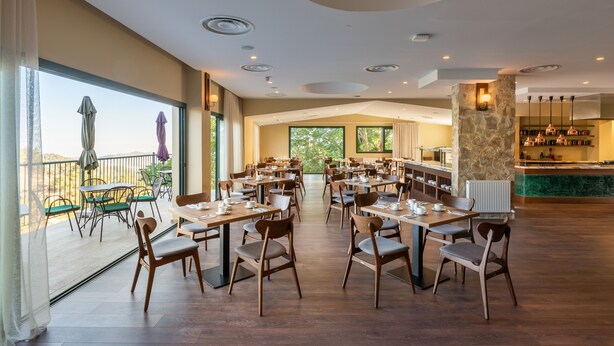 Un comedor amplio con varias mesas y sillas, ventanas grandes que ofrecen vistas al exterior y una pared de piedra decorativa con barra integrada.
