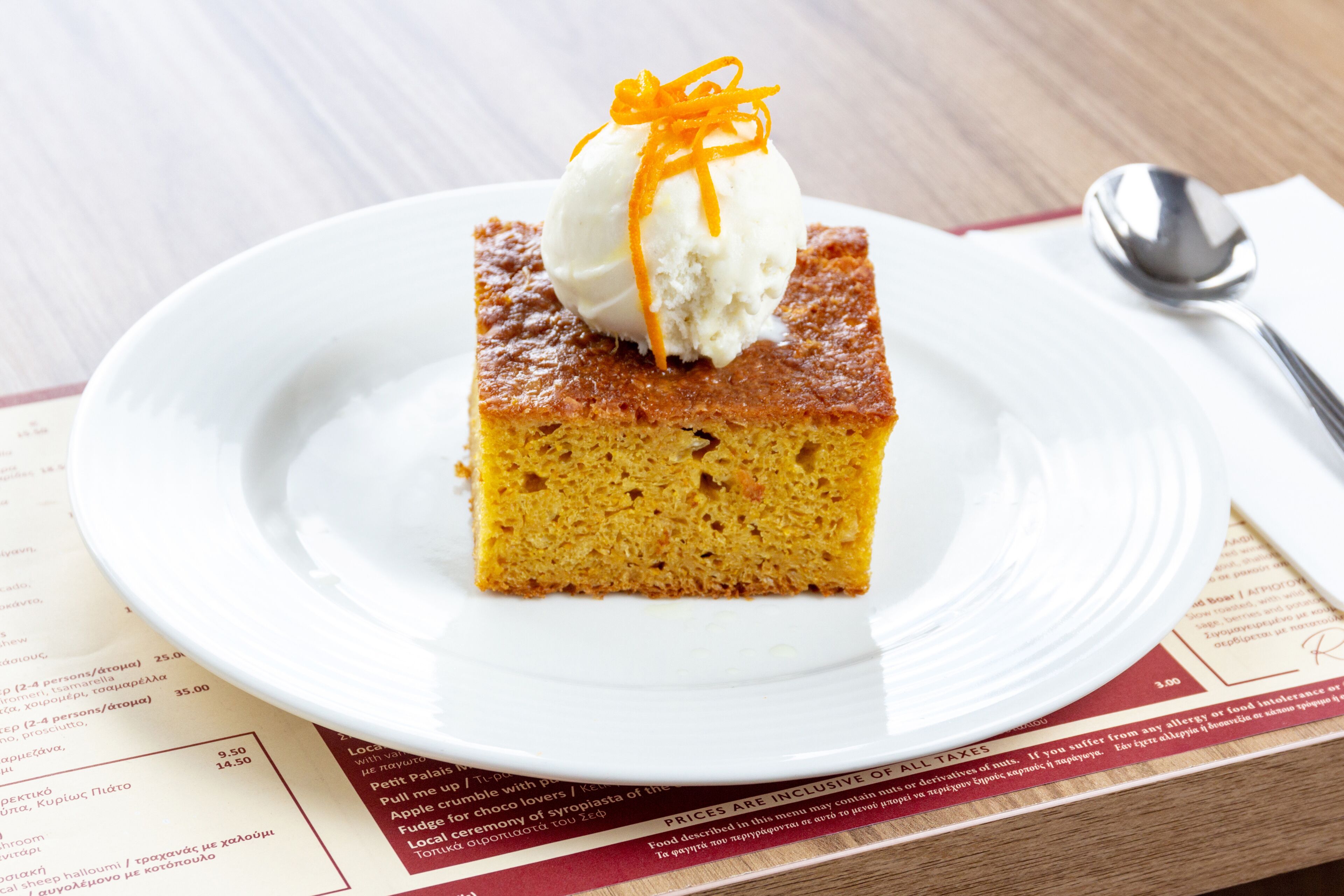 A slice of cake with a scoop of ice cream and a carrot garnish on a white plate.