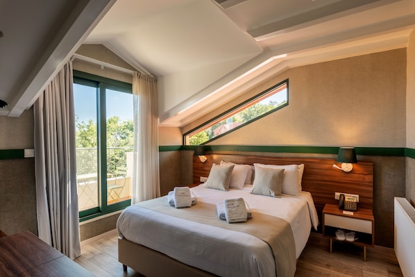 A hotel room with a large bed, a nightstand with a lamp, and a view of the outdoors through a window.