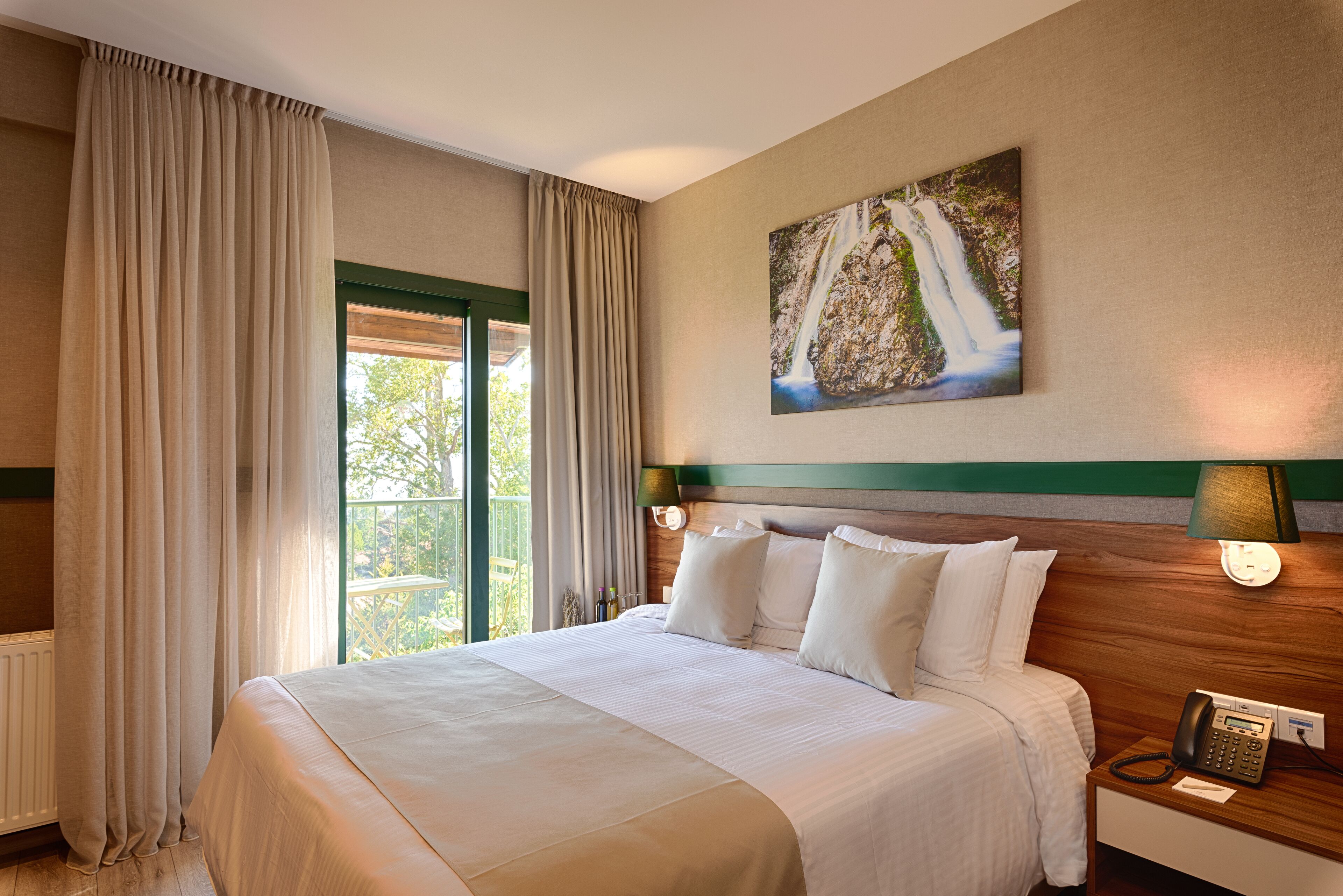 Una camera d'albergo con un letto grande, vista sul verde all'esterno, un quadro appeso al muro e un telefono sul comodino.